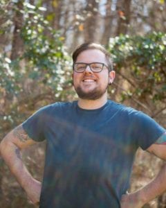 Man standing outside with his hands on his hips, smiling.