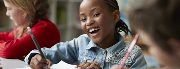 A young girl smiling working on school work with good children's mental health