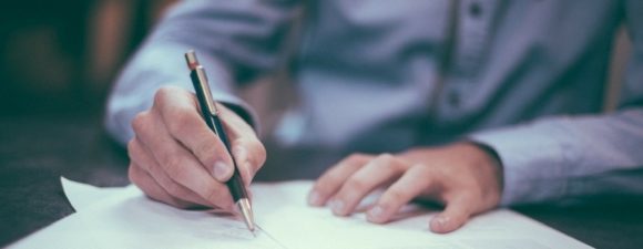 man writing on paper with pen