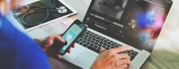 nurse holding phone while using laptop to take continuing education in healthcare classes