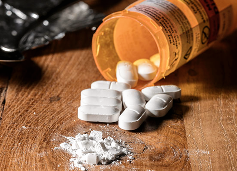 Photograph of a spilled bottle of pills with one crushed into dust in the foreground